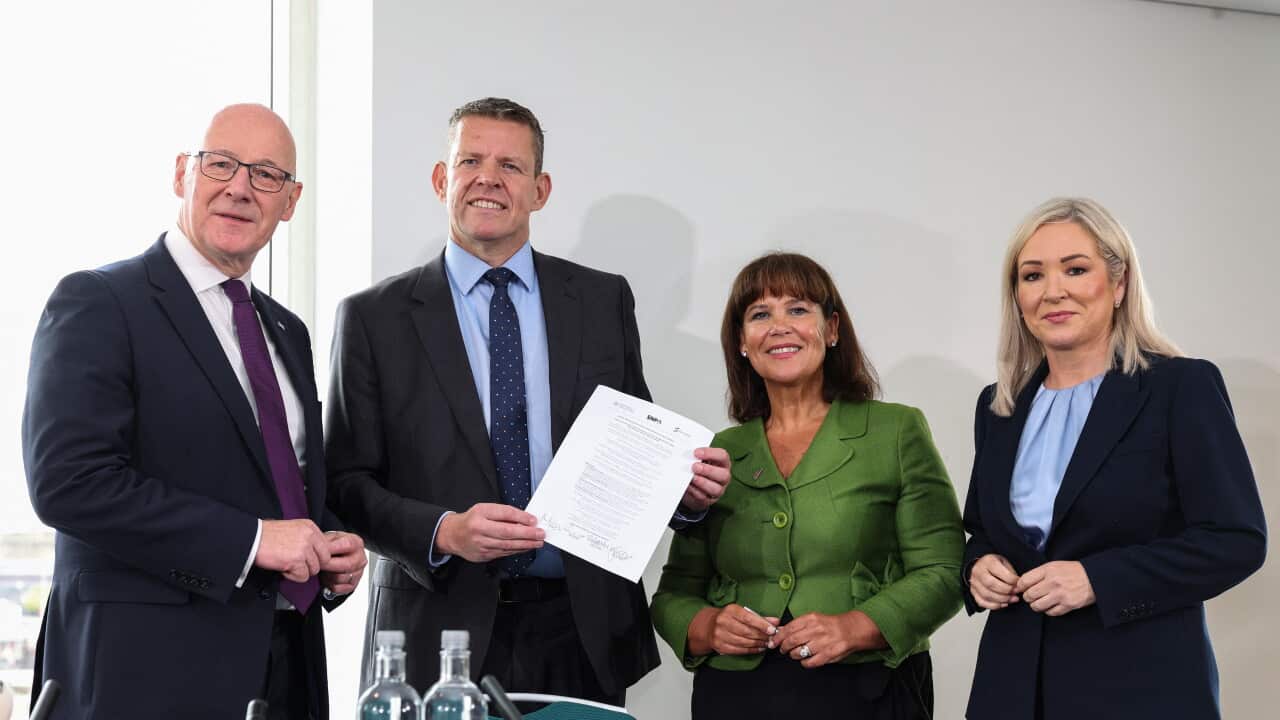 Two men and two women pose for a photo. One of the men is holding up a document.