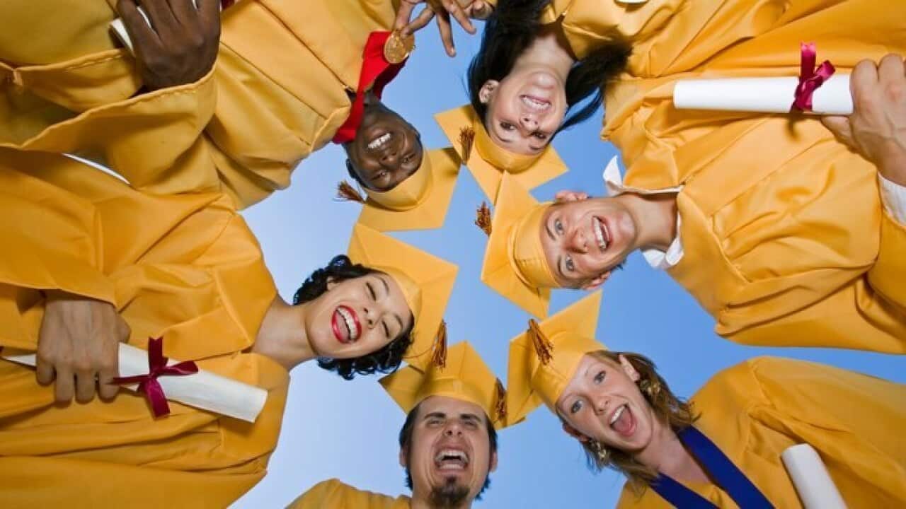 Group of graduates holding diplomas outside view from below