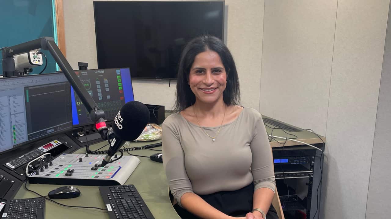 Dr Sitanshu Arora is sitting in SBS studios in Melbourne with a mic in front of her face, some screens behind her.