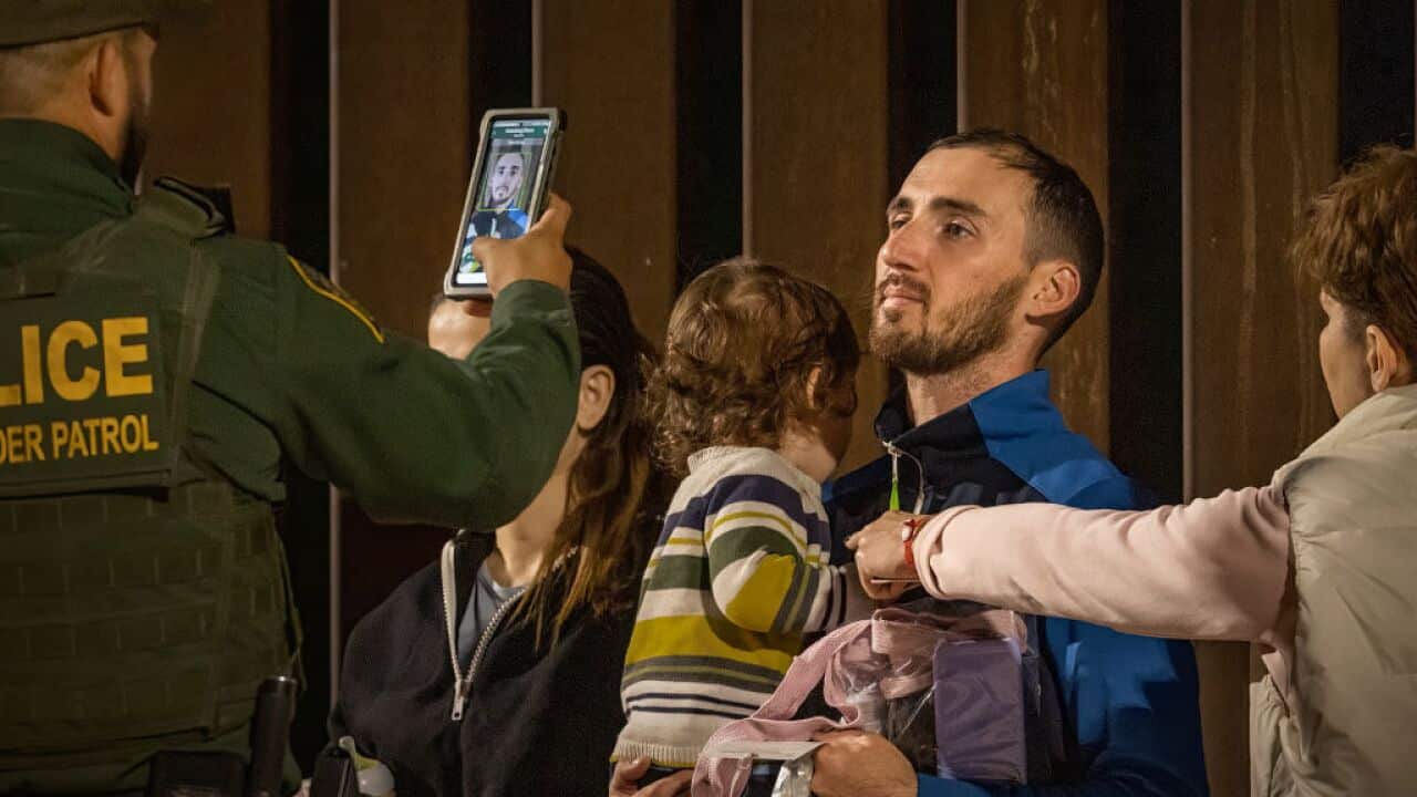 An officer photographs a man holding a child for immigration processing