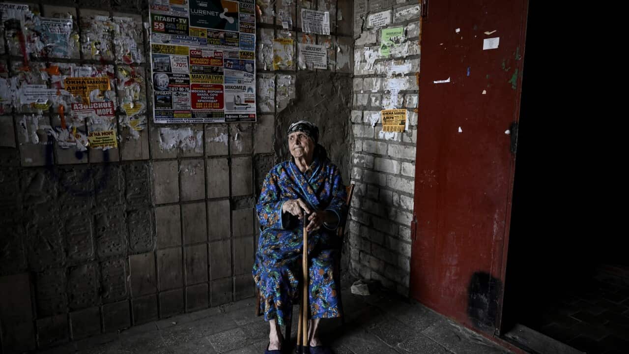 An old woman sits in the corner of a building.