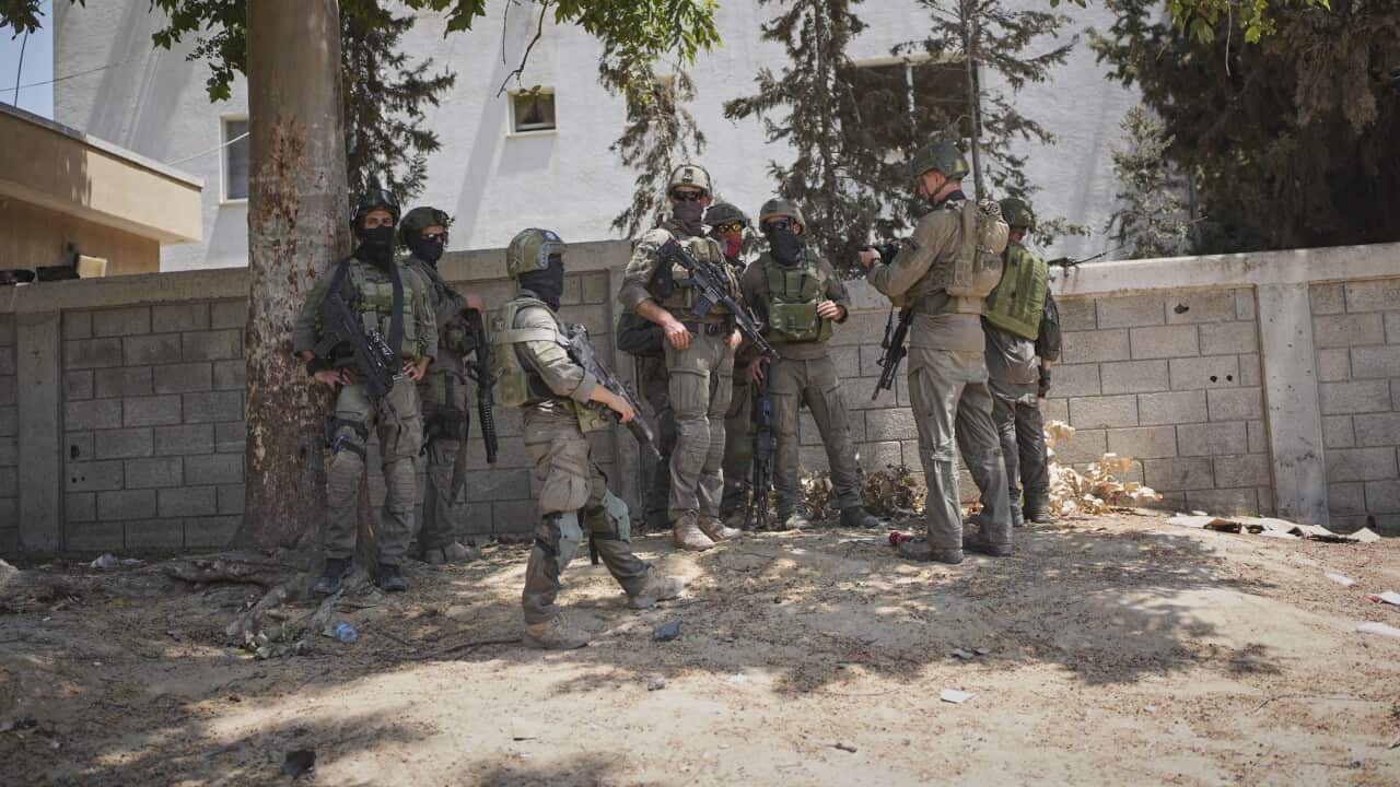 A group of soldiers gathers near a cinderblock wall.