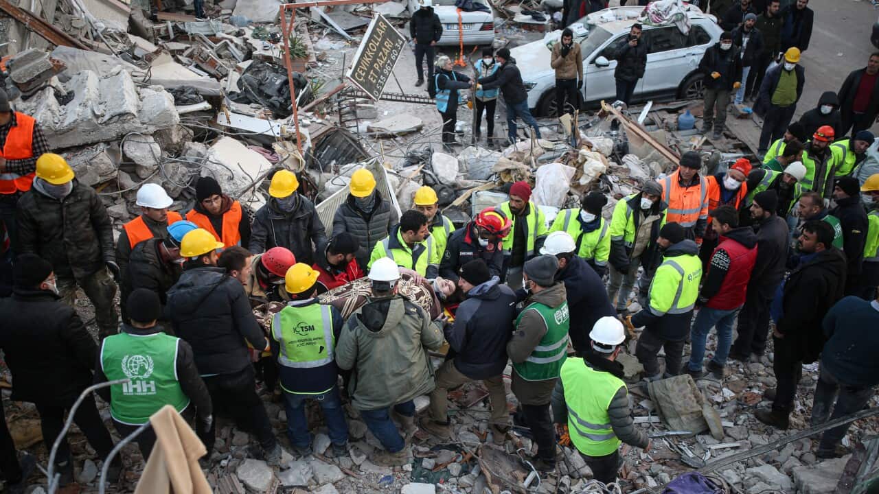 A woman is carried on a stretcher by search and rescue crews. Rubble from damaged buildings is all around them.