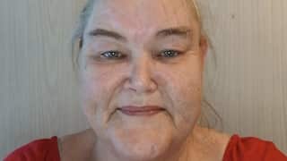 A picture of a woman with grey hair tied up in a bun, smiling lightly at the camera. A picture is on the wall in the background.