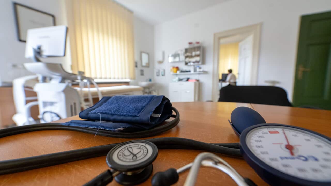 A photograph of a doctor's office. A stethoscope and blood pressure armband sit on a desk.