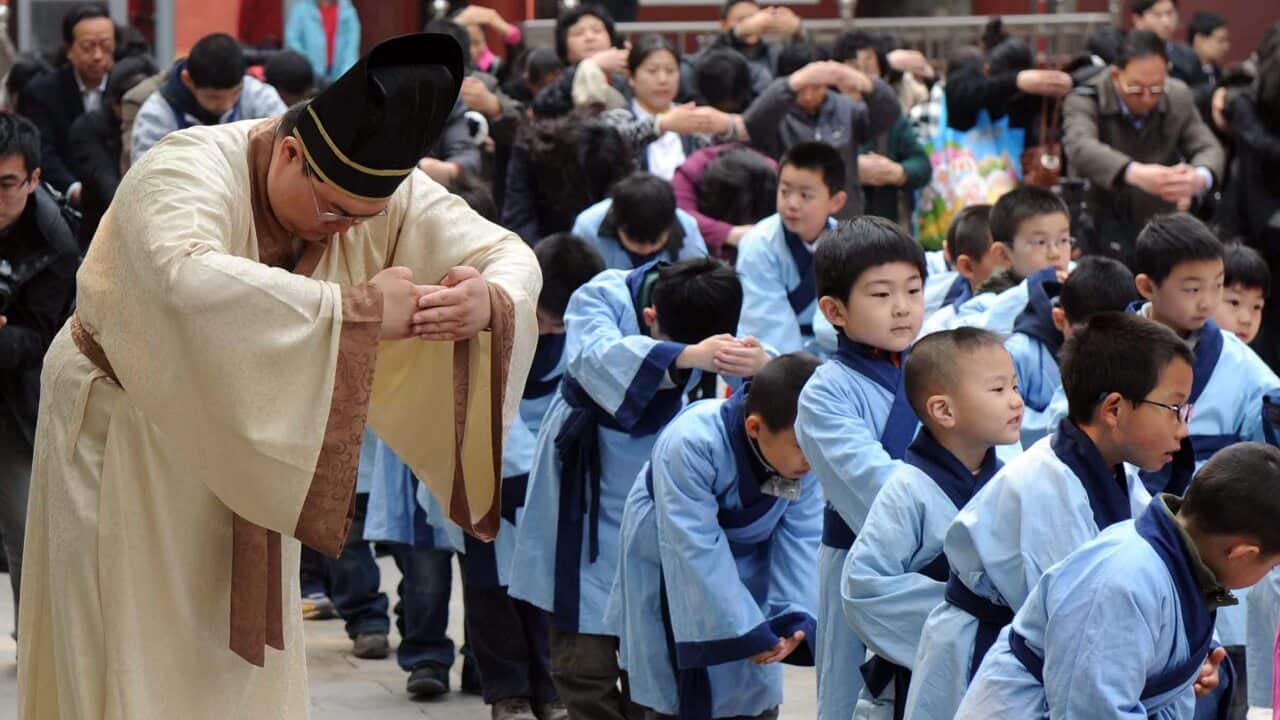 A teacher leads a group of young Chinese children dressed in ancient costumes, to pay homage to the statue of Confucius, at the Confucius temple in Beijing.