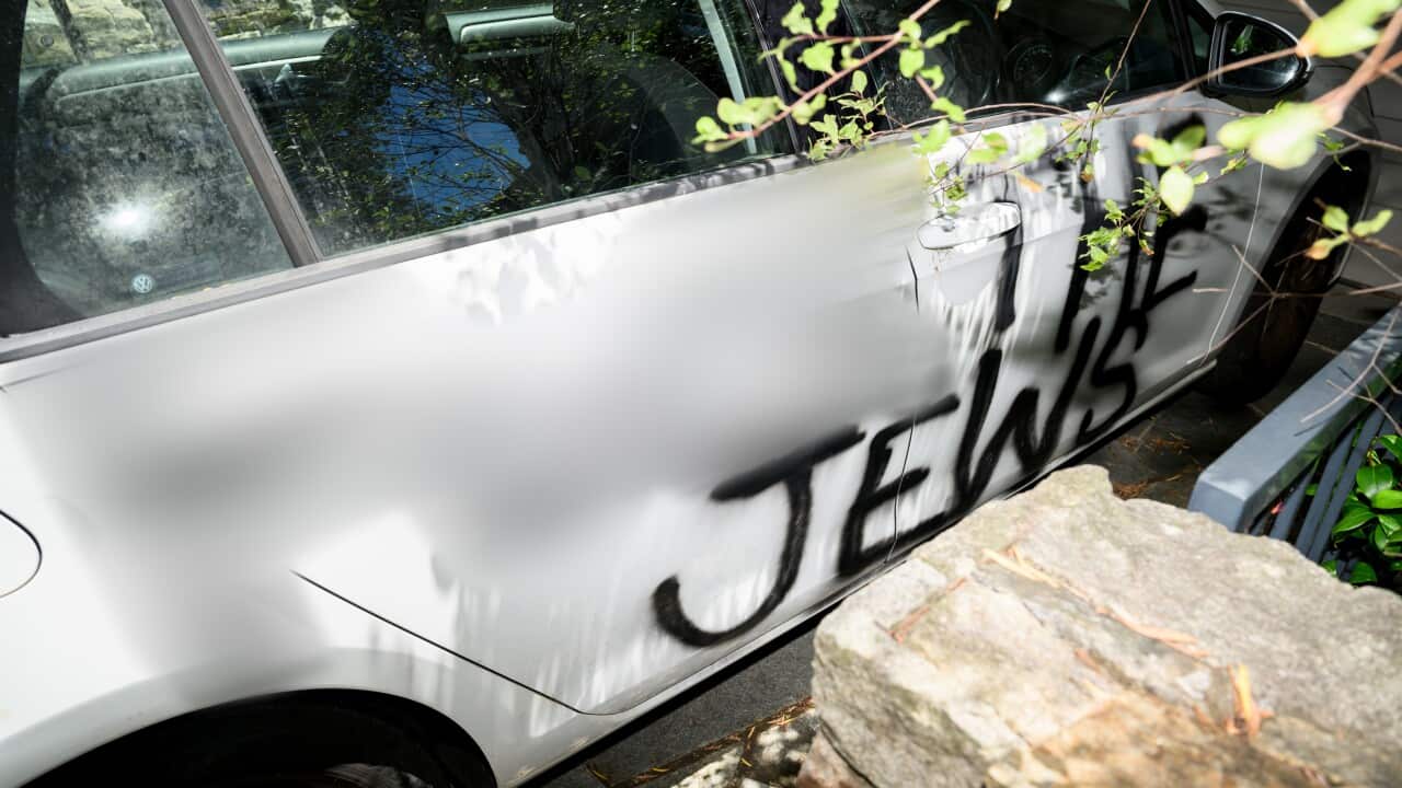 A white car with the words "The Jews" spray painted on the side. A word preceding that phrase has been blurred out.