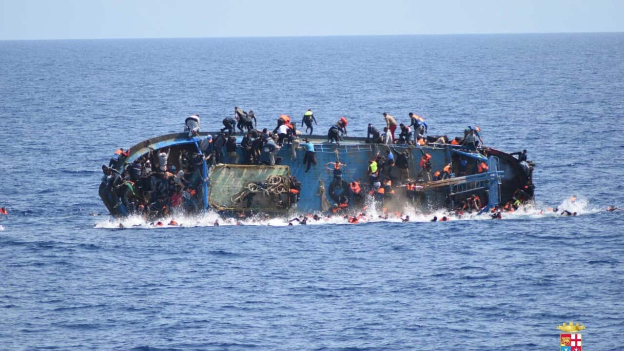A handout picture released by the Italian Navy shows people jumping out of a boat right before it overturns in Canal of Sicily off the Libyan coast