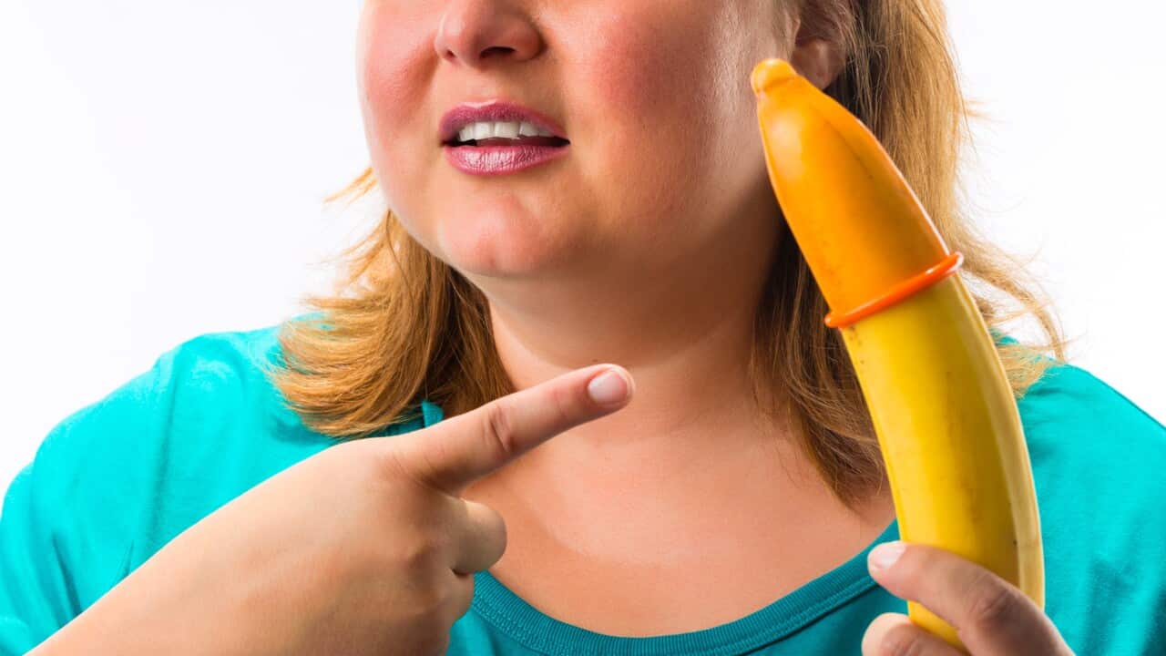 Young woman holding banana with condom - she looks confused