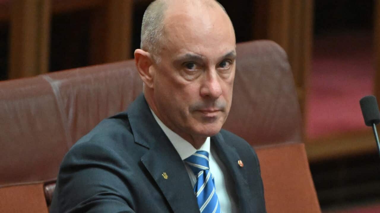 A man seated at a desk in front of a microphone.