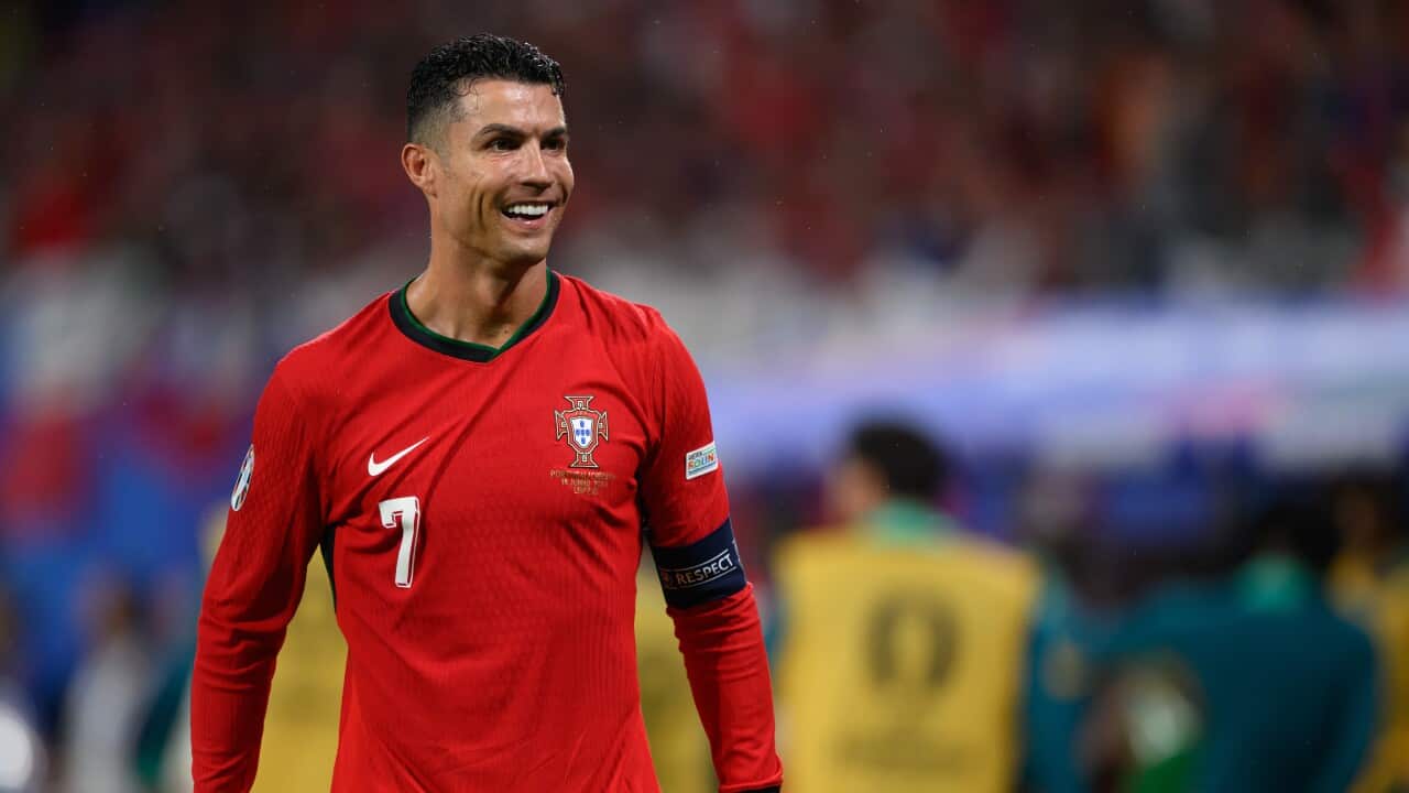 Cristiano Ronaldo, wearing a red long-sleeved shirt, smiles as he looks sideways.