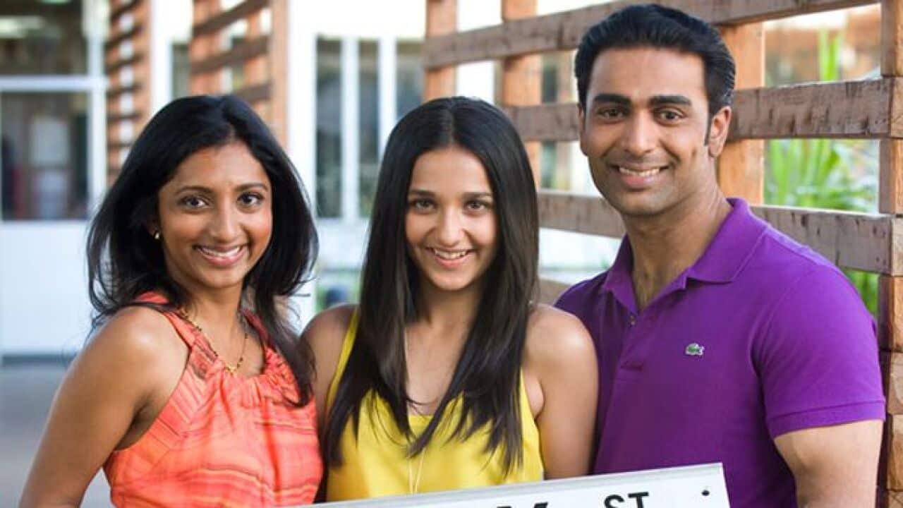Three people holding a Ramsay St sign.