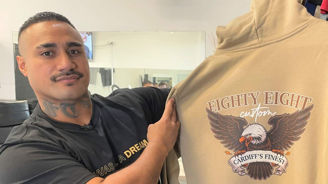 Kinahoi holding up a printed sweat-shirt in his barber shop.