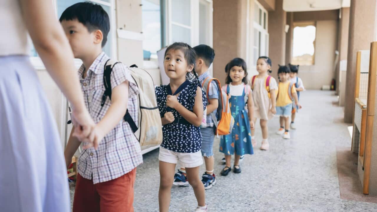 Preschool teacher guiding and arranging students waiting in line entering classroom