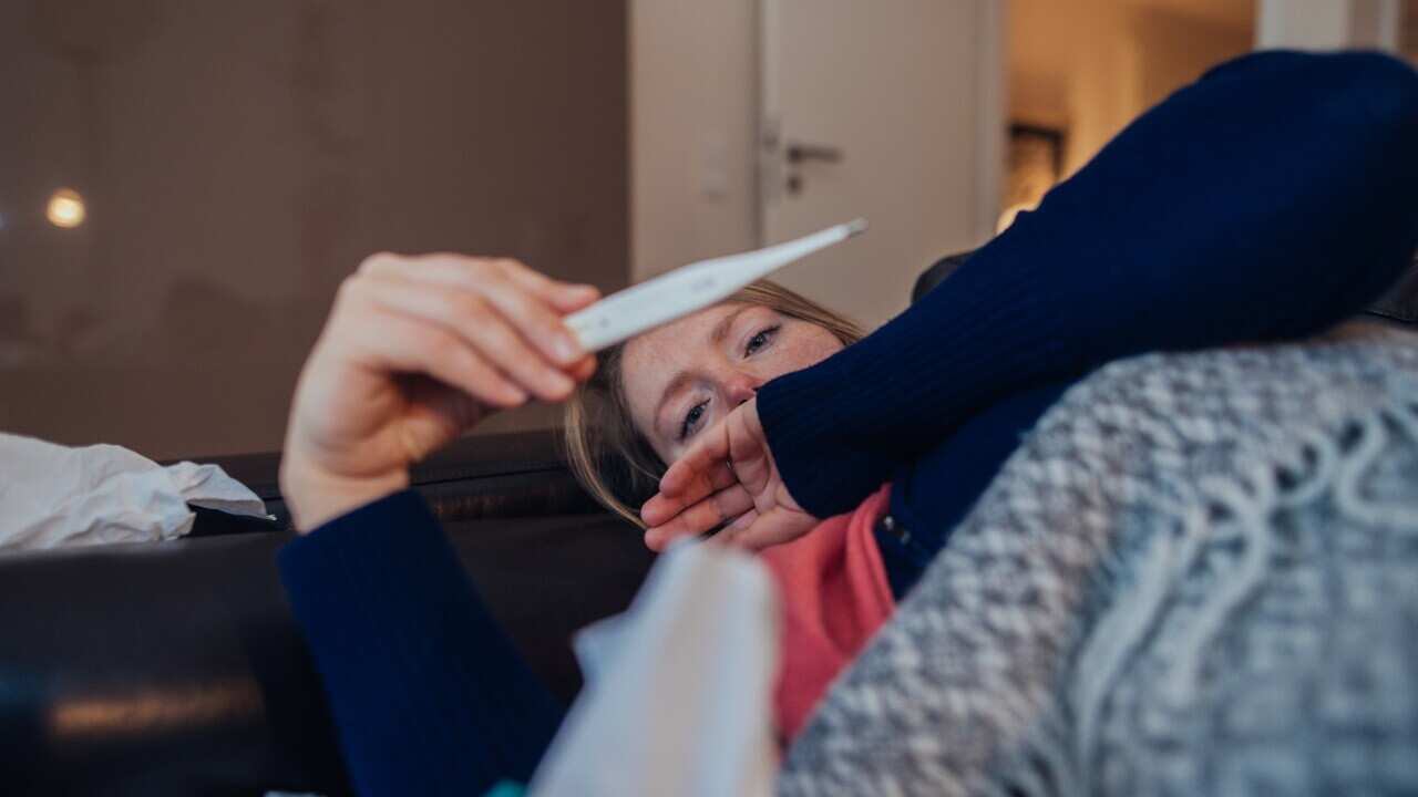 Ill woman looking at thermometer.