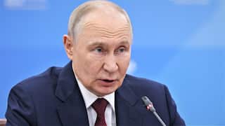 Vladimir Putin looks stern while speaking into a microphone