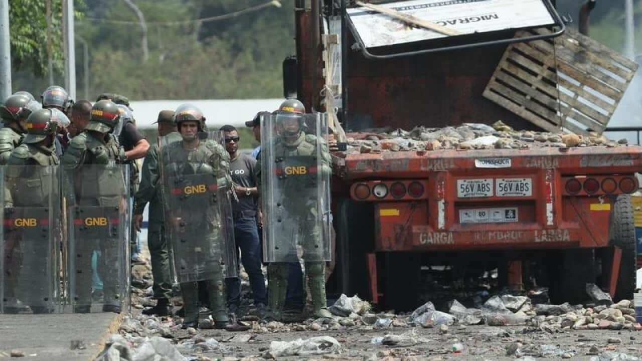 Troops stand ready next to a wrecked lorry on a bridge