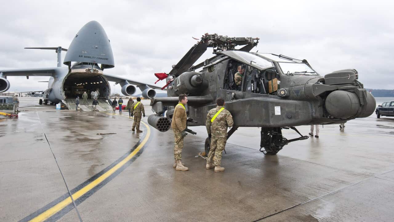 A helicopter in front of a transport plane with military personnel around it