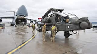 A helicopter in front of a transport plane with military personnel around it