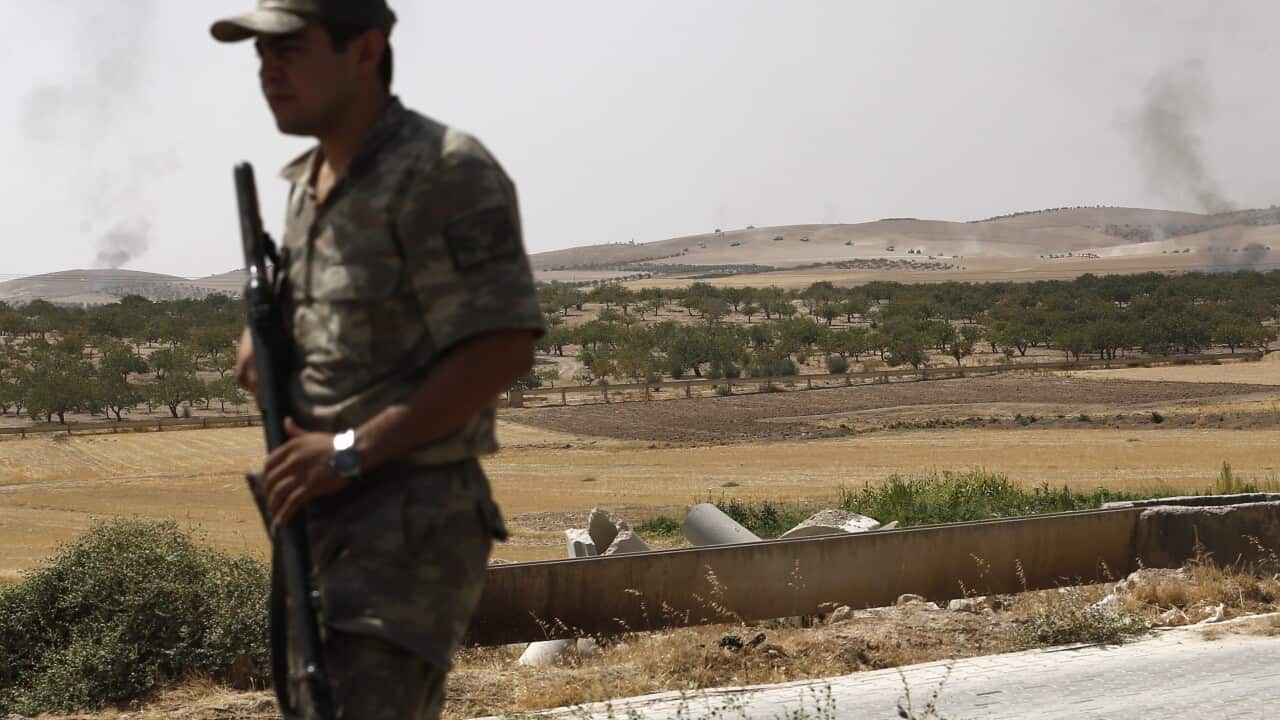 Military personnel looks on while smoke raises in the background as Turkish pass the Syrian border as part of the offensive against the so-called Islamic State