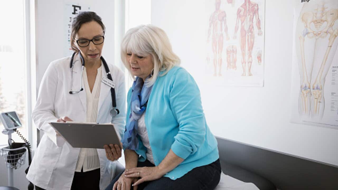 Female doctor and senior patient reviewing medical chart in clinic examination room