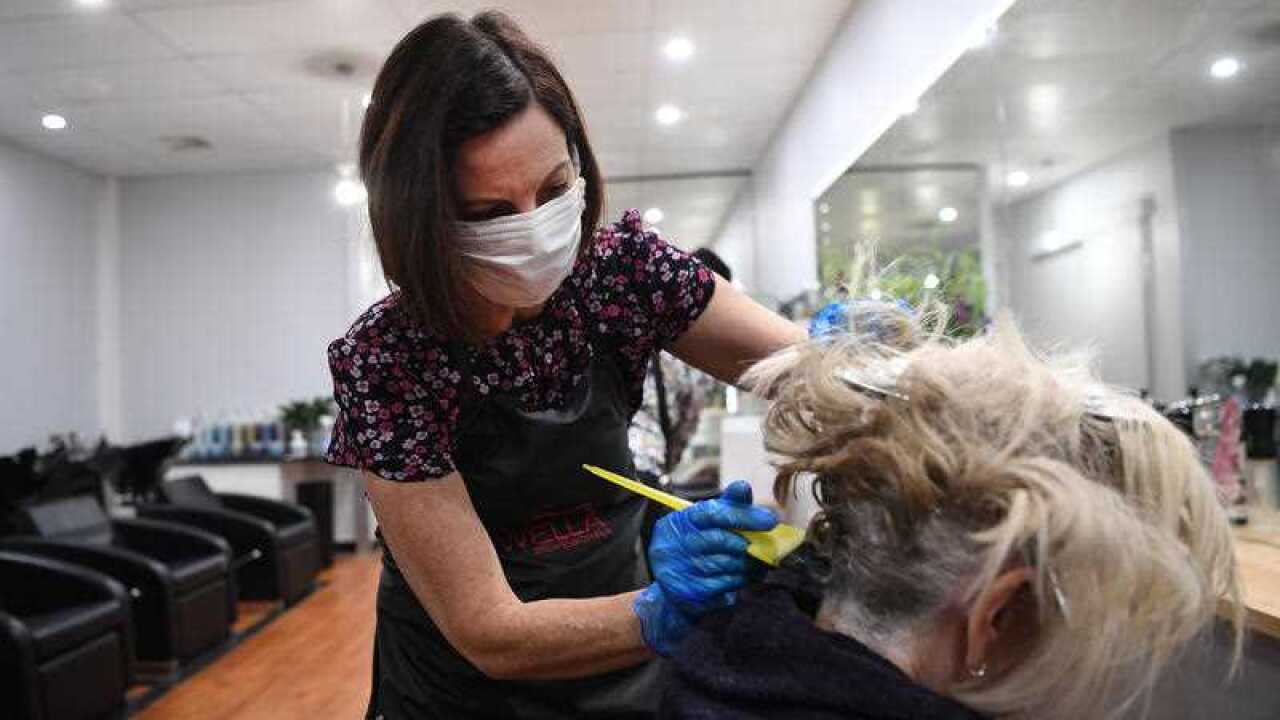 A hairdresser in a floral top combs a client's blonde hair