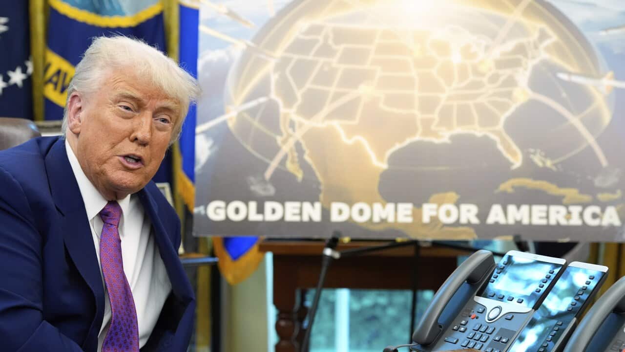 Donald Trump talks in front of a globe poster with the words "Golden dome for America" written on it. There's a phone in front of him.