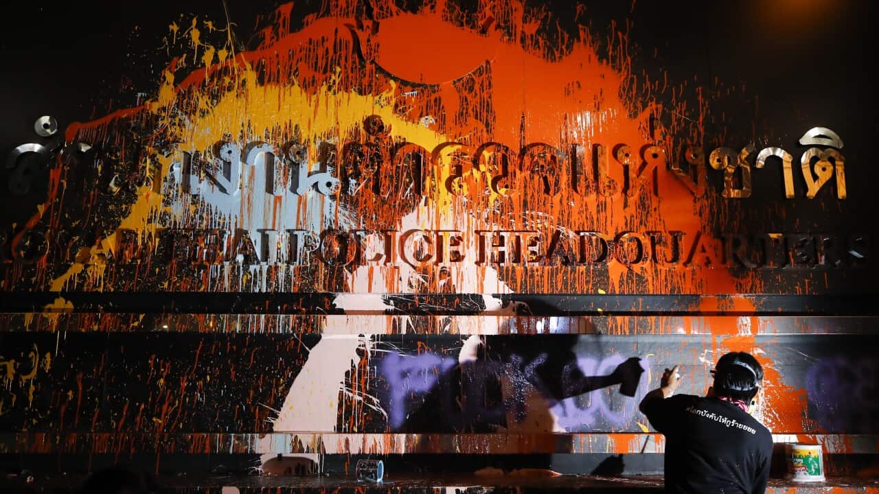 A pro-democracy protester spray paints the royal Thai police headquarters' sign during a protest calling for political and monarchy reform in Bangkok.