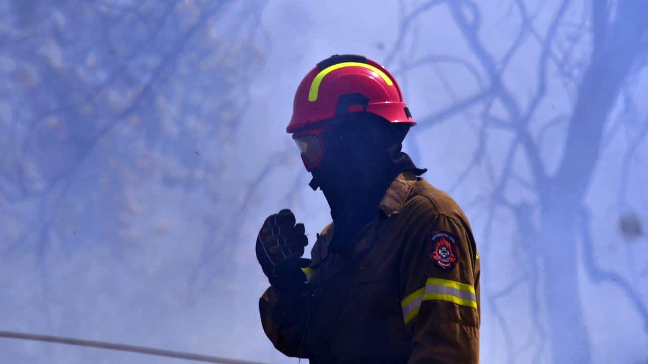 A firefighter with protective equipment stands surrounded by smoke.