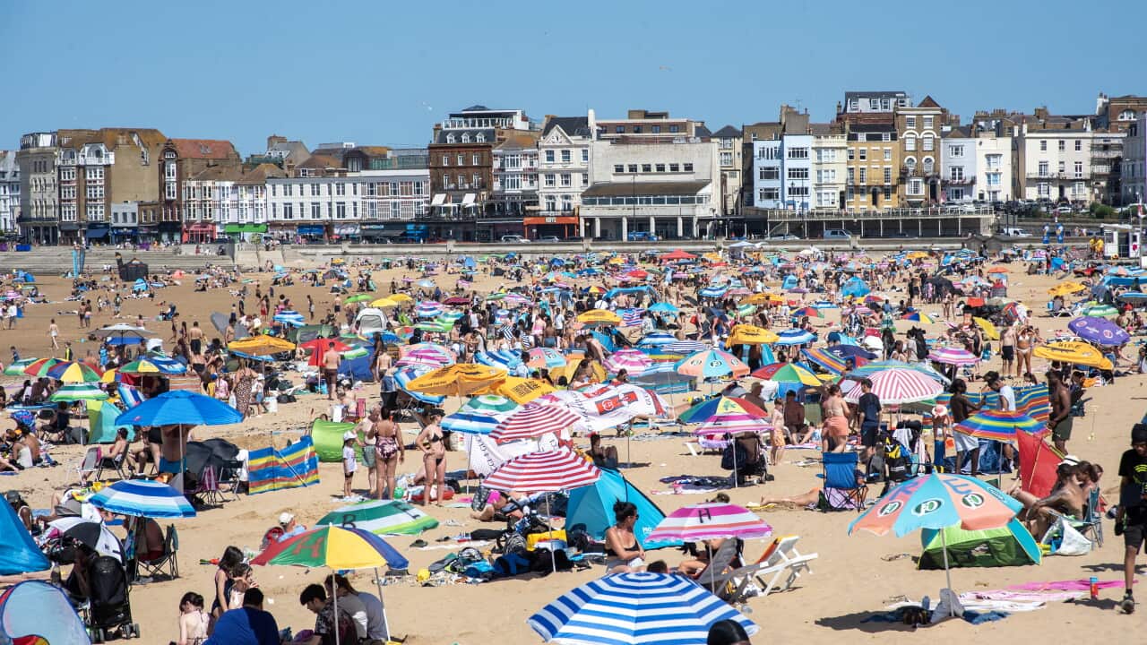 Hundreds of people on a beach with umbrellas and chairs on a clear sunny day.
