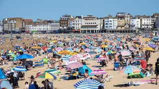 Hundreds of people on a beach with umbrellas and chairs on a clear sunny day.