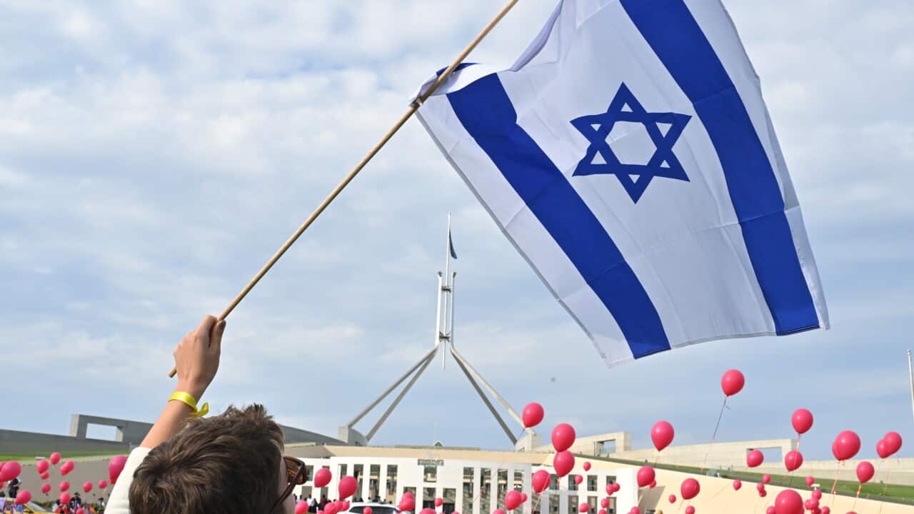 A person flies an Israeli flag with red balloons seen in the background.