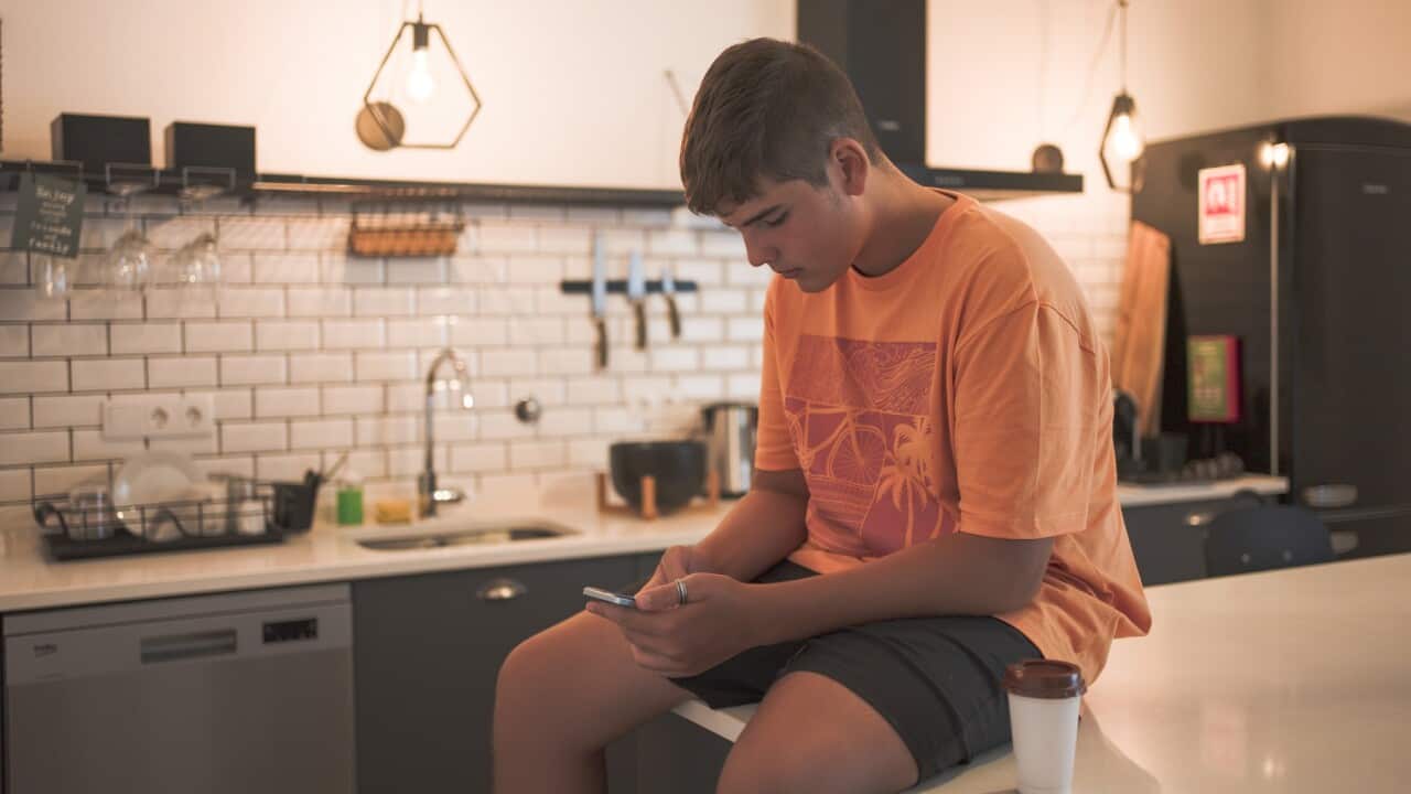 Teenage boy sitting at the kitchen table interacting with his smart phone while having a takeaway coffee