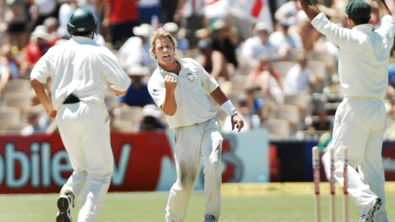 Cricketer Shane Warne celebrates on the pitch as he is surounded by team mates.
