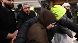 A group of people assist a woman wearing a headscarf as she's ushered through an airport terminal.