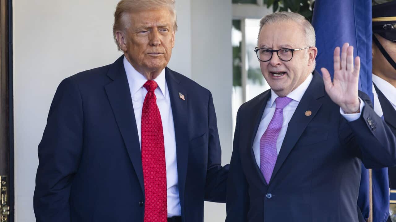 Donald Trump standing next to Anthony Albanese, who is waving a hand. They are in front of a white wall.