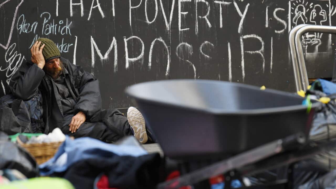 A homeless man sits on the ground as others pack away their belongings