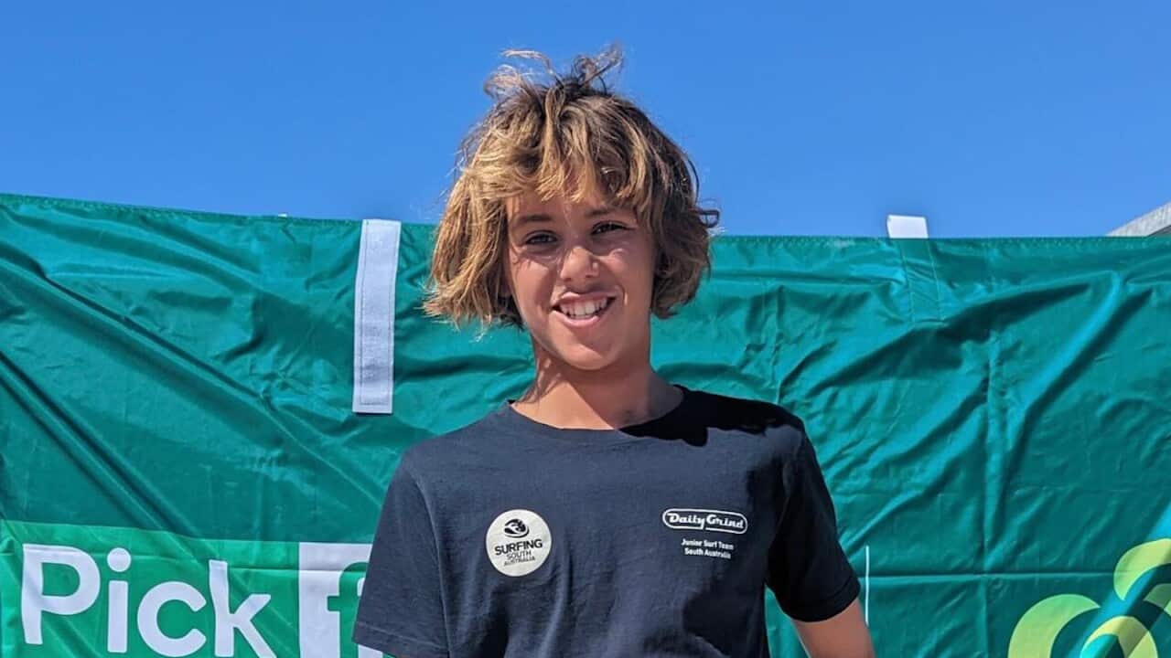 A teenage boy with blonde hair smiling in front of a green banner.