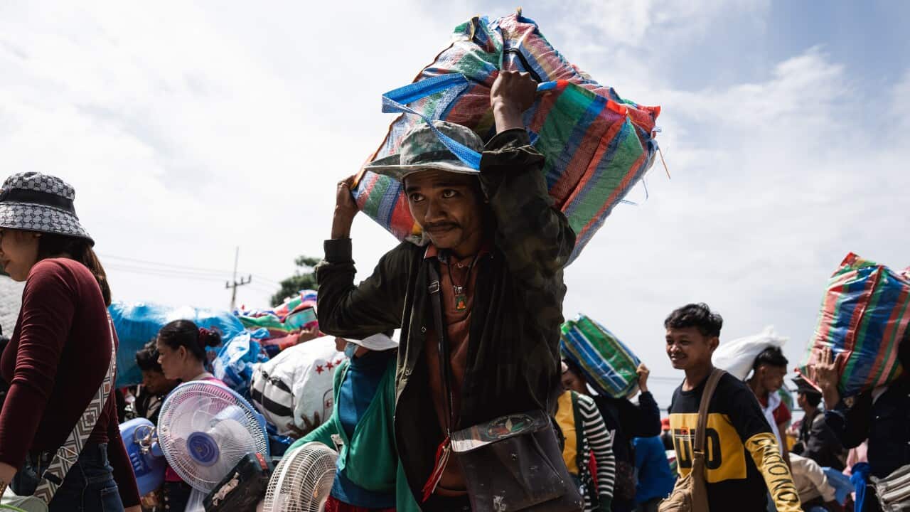 A man carrying a large bag of possessions on his shoulders, in front of a crowd