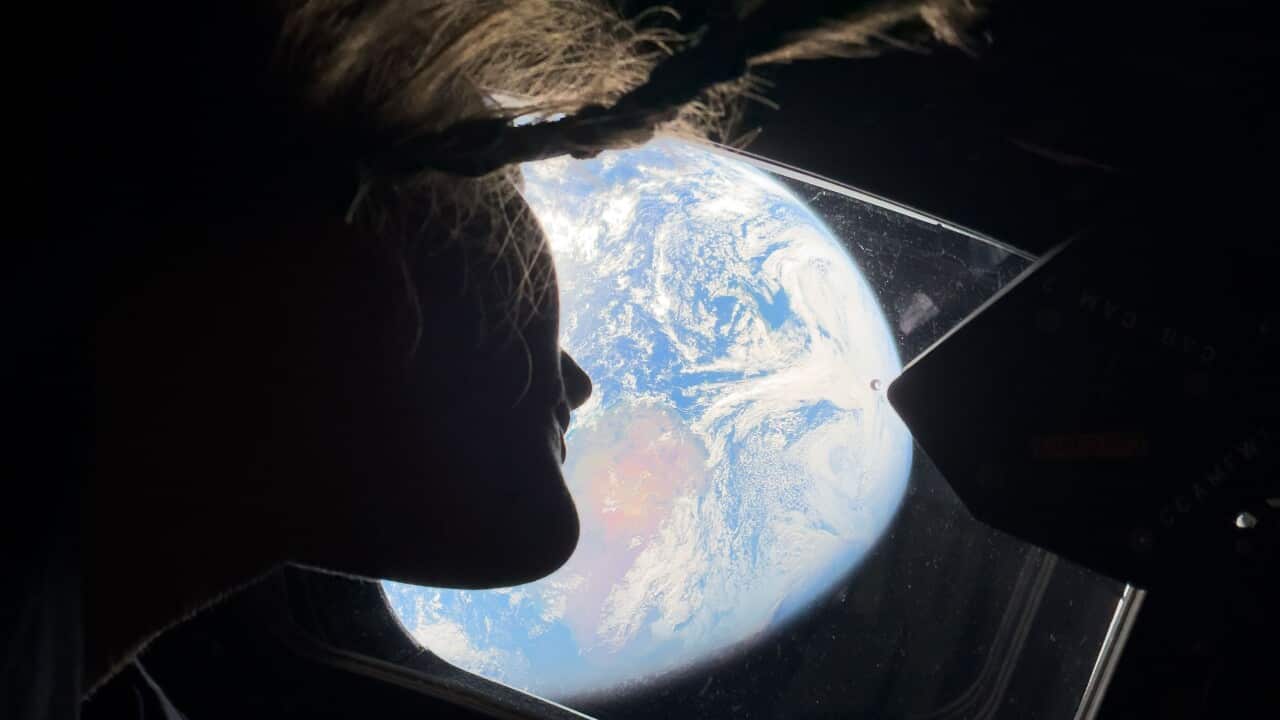 A view of Earth taken from the window of a spacecraft, partially obscured by a person's silhouette