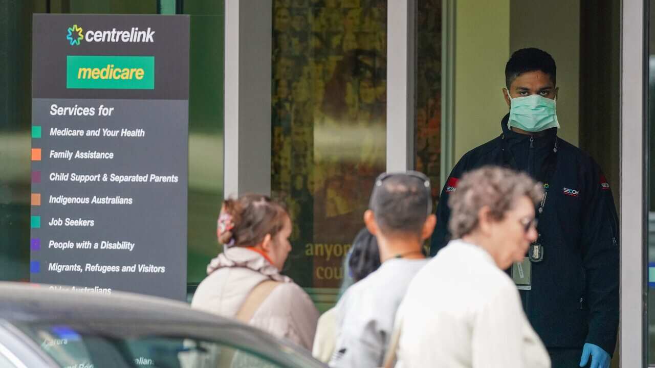 A security guard looks on as people are seen in long queue outside a Centrelink office in Abbotsford, Melbourne, Monday, 23 March, 2020.