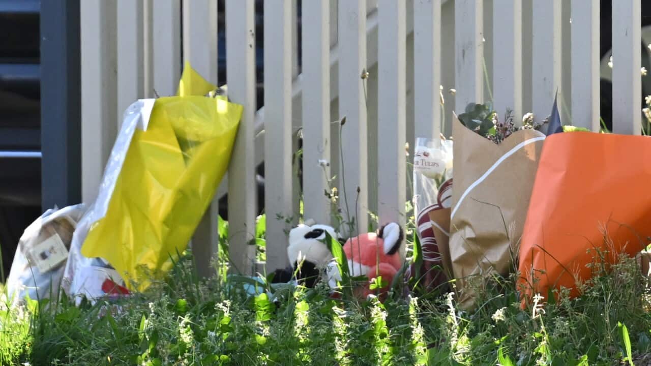 Flowers and other tributes up against a fence.