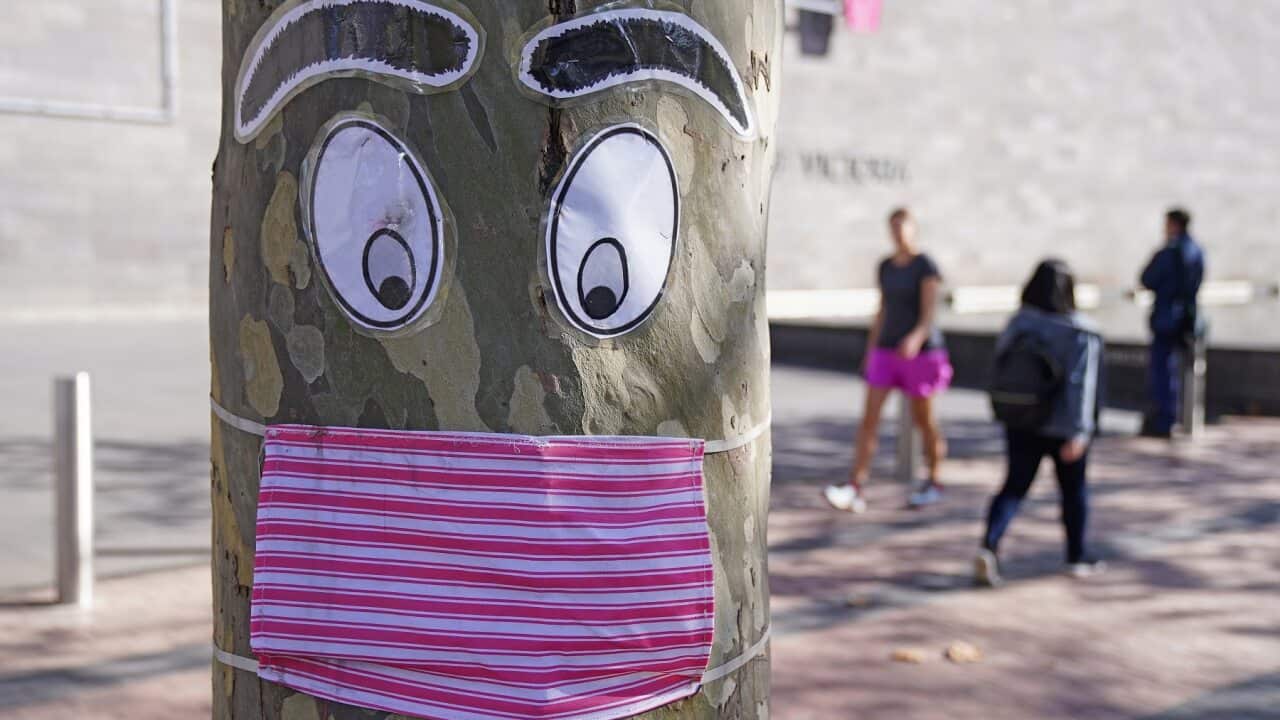 People walk past a tree with a face mask and eyes stapled to it in Melbourne.