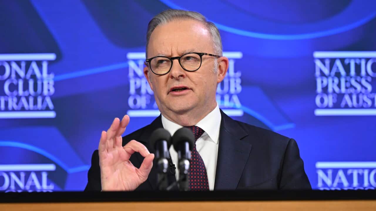 A middle-aged white man wearing a dark suit and lectern speaking before a lectern