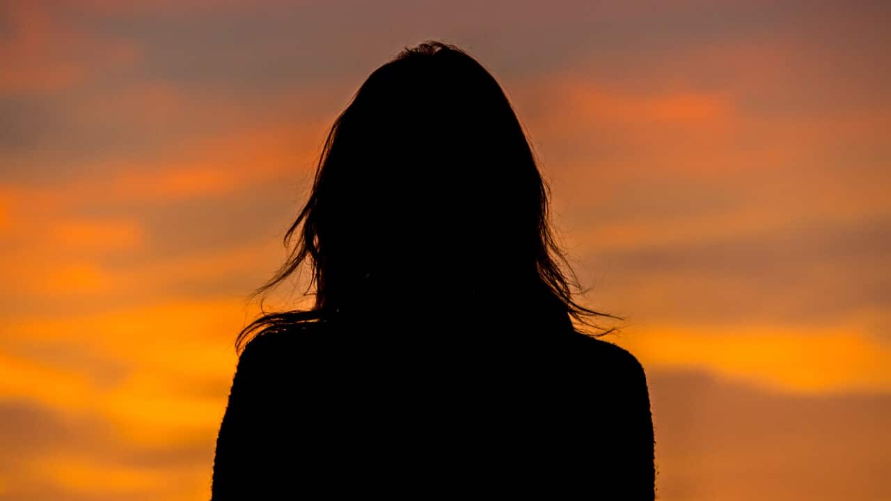 Silhouette of a woman standing against orange sky during sunset.