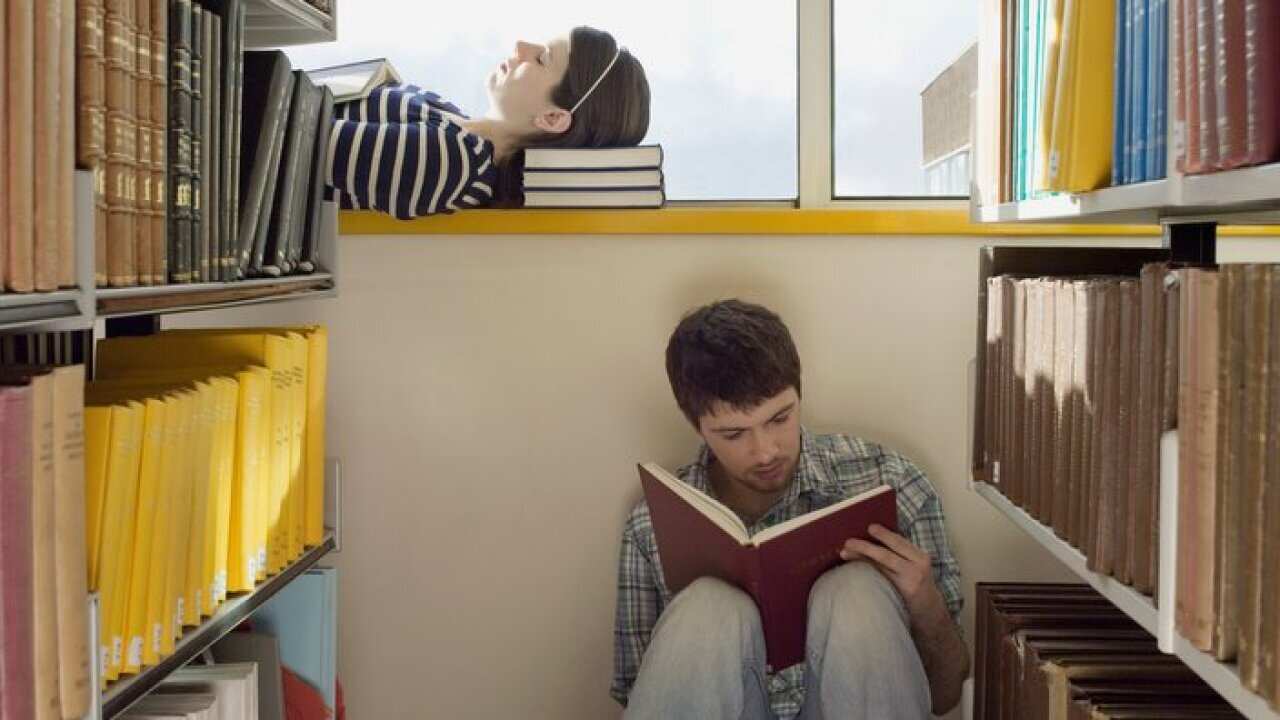 Female student lying down on library windowsill male student sitting on library floor reading