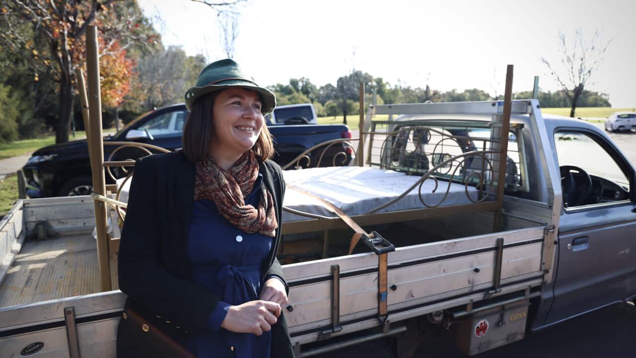 A middle-aged woman, wearing a coat and a hat, leans beside the tray of her vehicle, smiling at the camera.