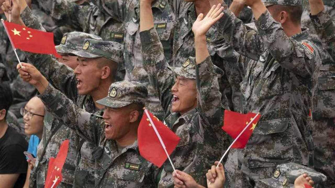 Chinese PLA soldiers hold national flags. The head of parliament's intelligence committee has warned Australia is facing an increased Chinese threat.