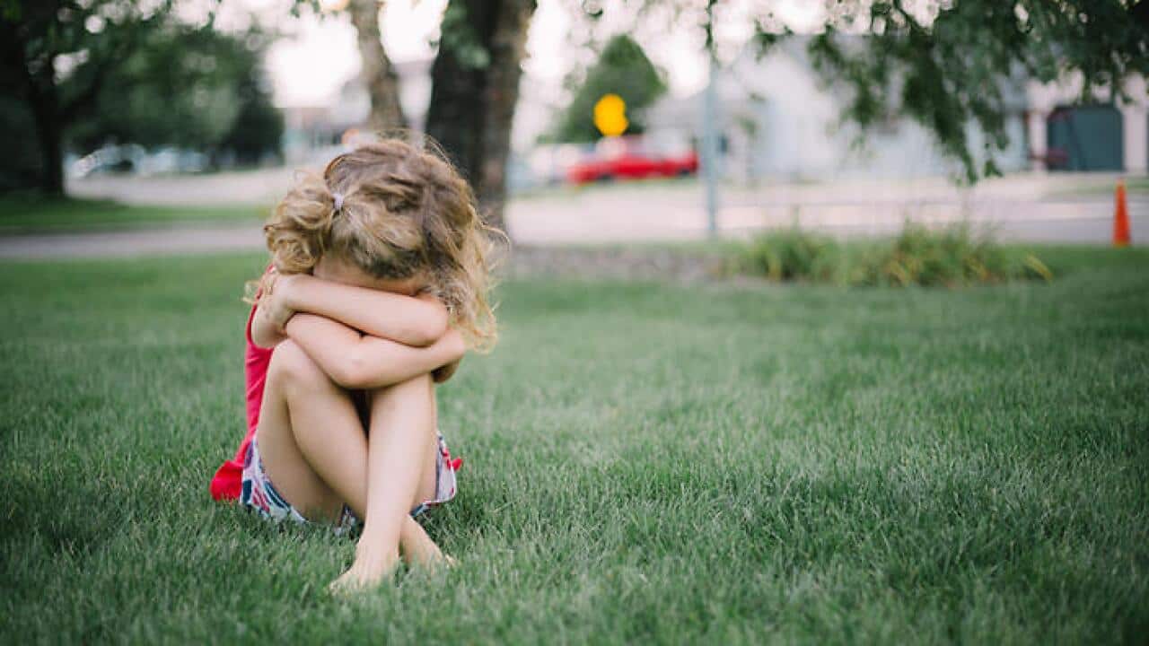 Little girl with curly hair sits on grass and cries into her arms.