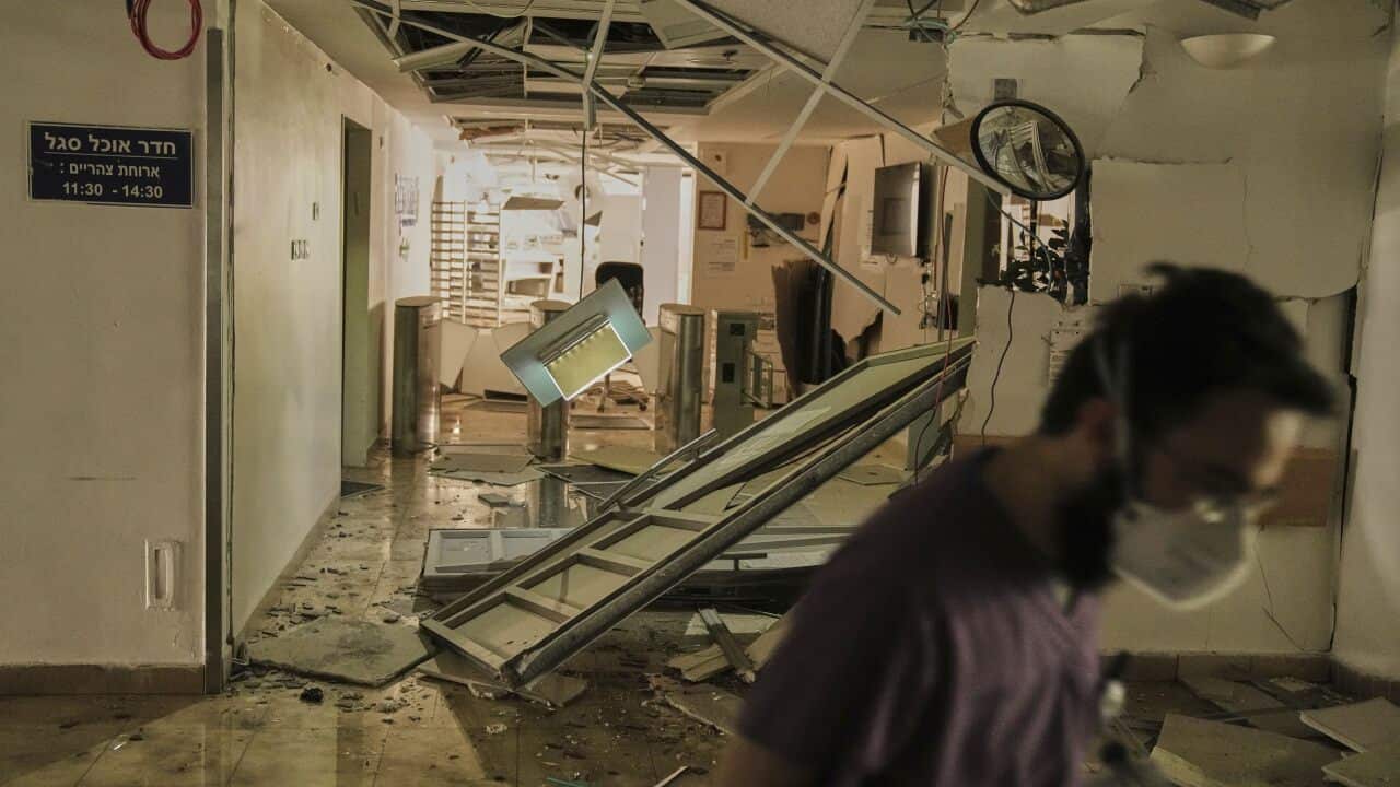 A medical staff member walking through a hallway of a building which has been damaged, with debris strewn across.